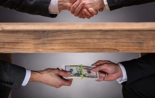 Business hand shake with money under the table committing corporate fraud