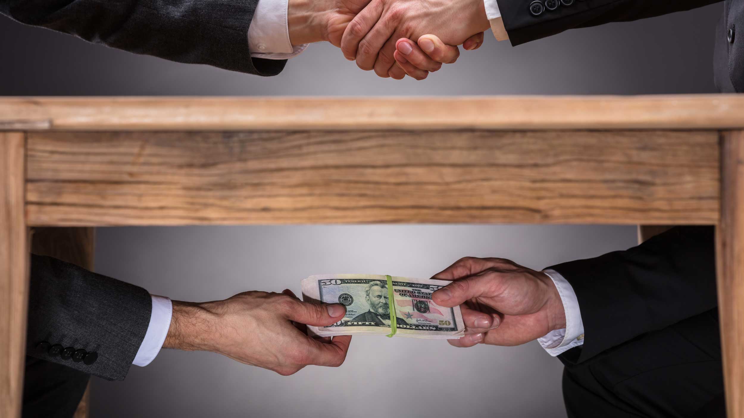 Business hand shake with money under the table committing corporate fraud