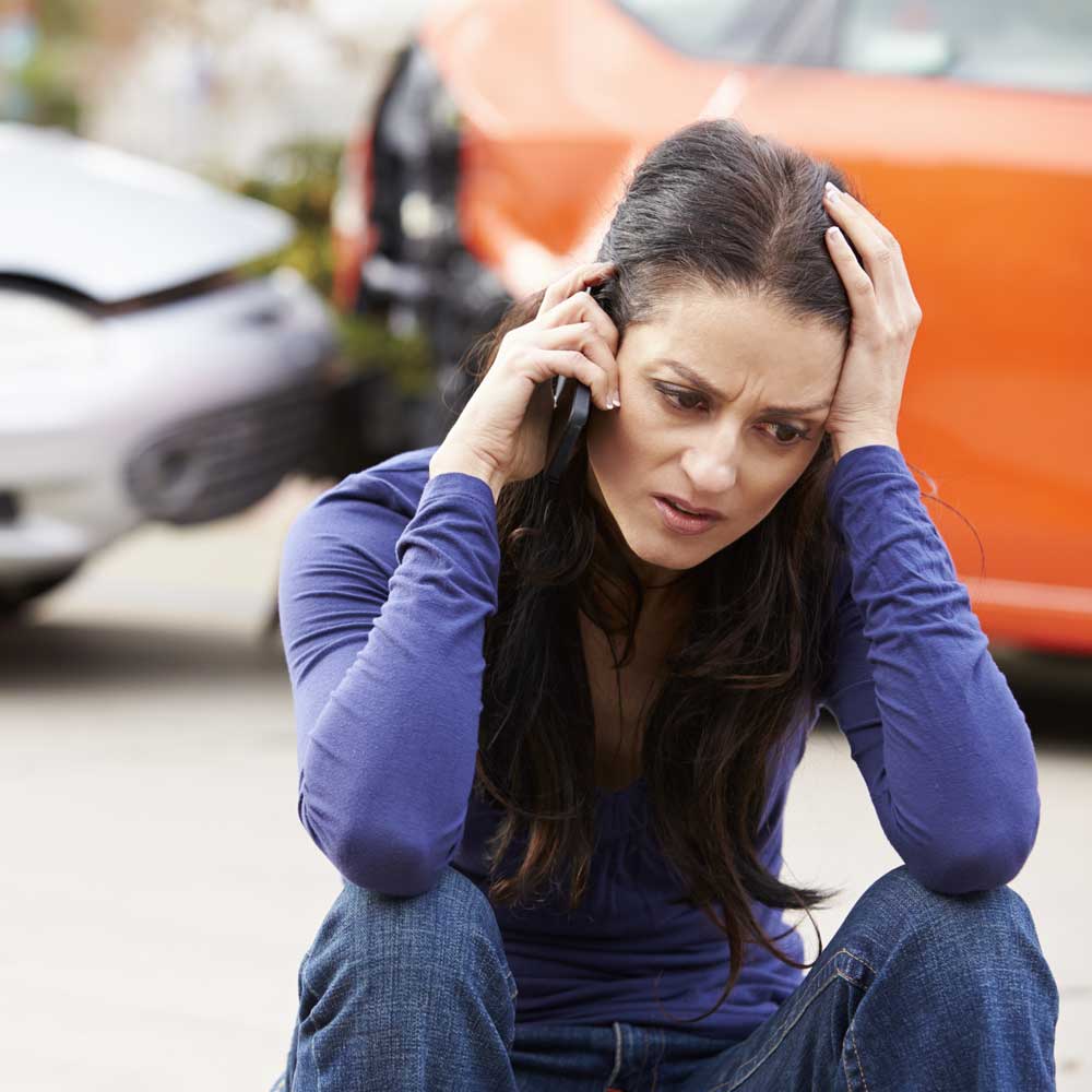 Woman sitting down in distress and calling 911 after a car accident