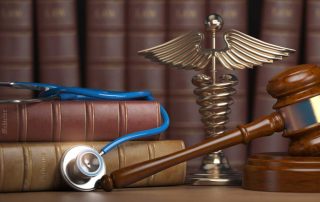 A judge’s gavel rests beside a stethoscope and a medical caduceus symbol in front of stacked law books, representing the intersection of law and healthcare.