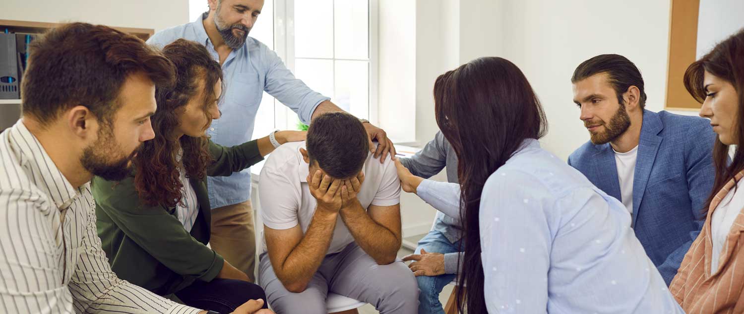 Man surround by friends crying over the loss of a loved one