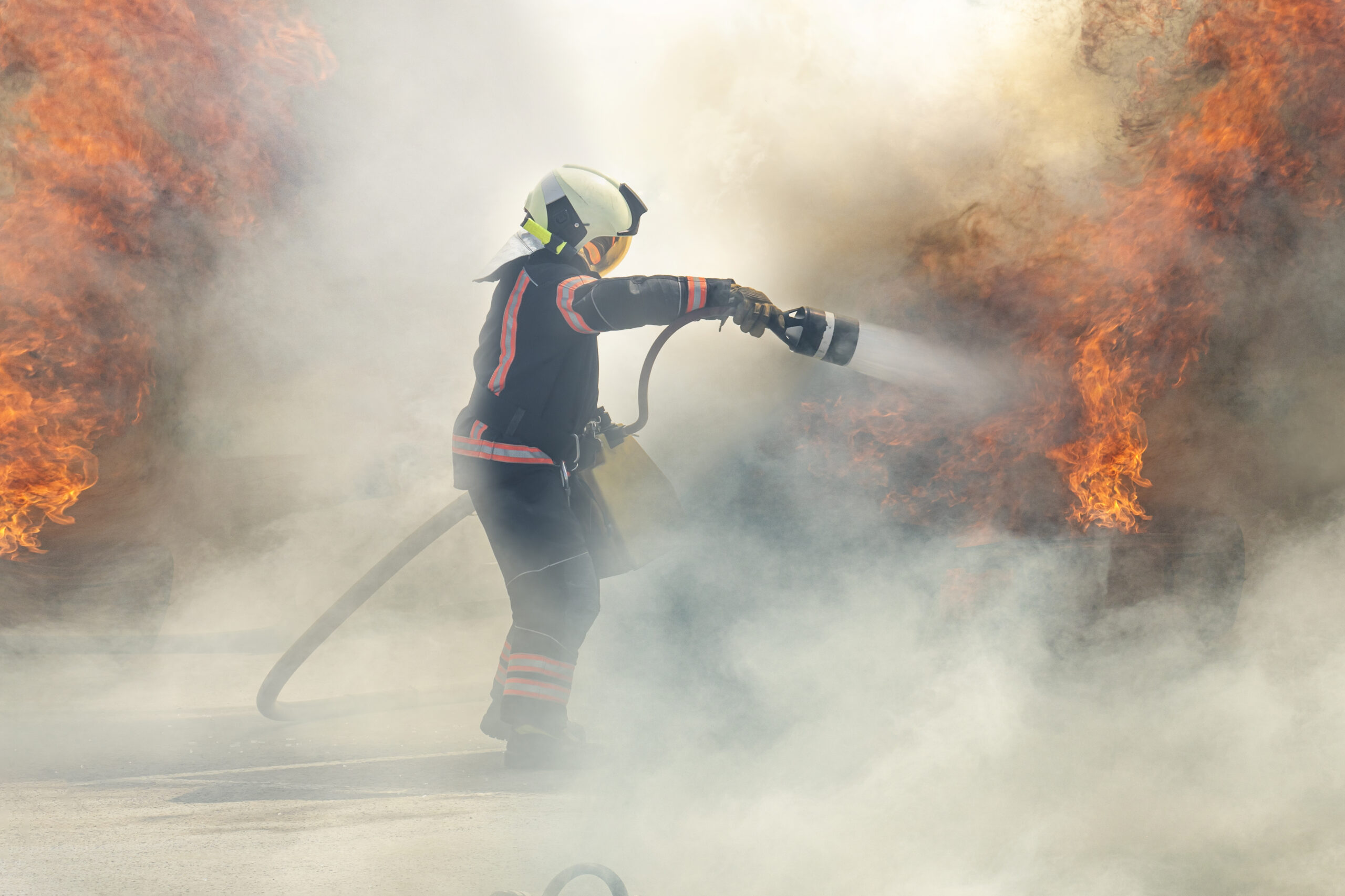 The hero firefighter stands among the smoke and fire and extinguishes the fire with a stream of water.. firefighter extinguishes a fire Firefighter sprays water on a fire